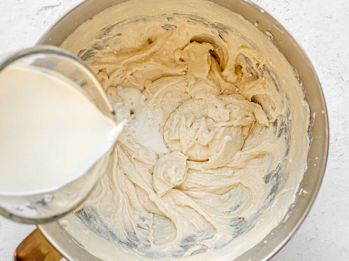 Unicorn Cupcakes pouring milk into cupcake batter in mixing bowl.