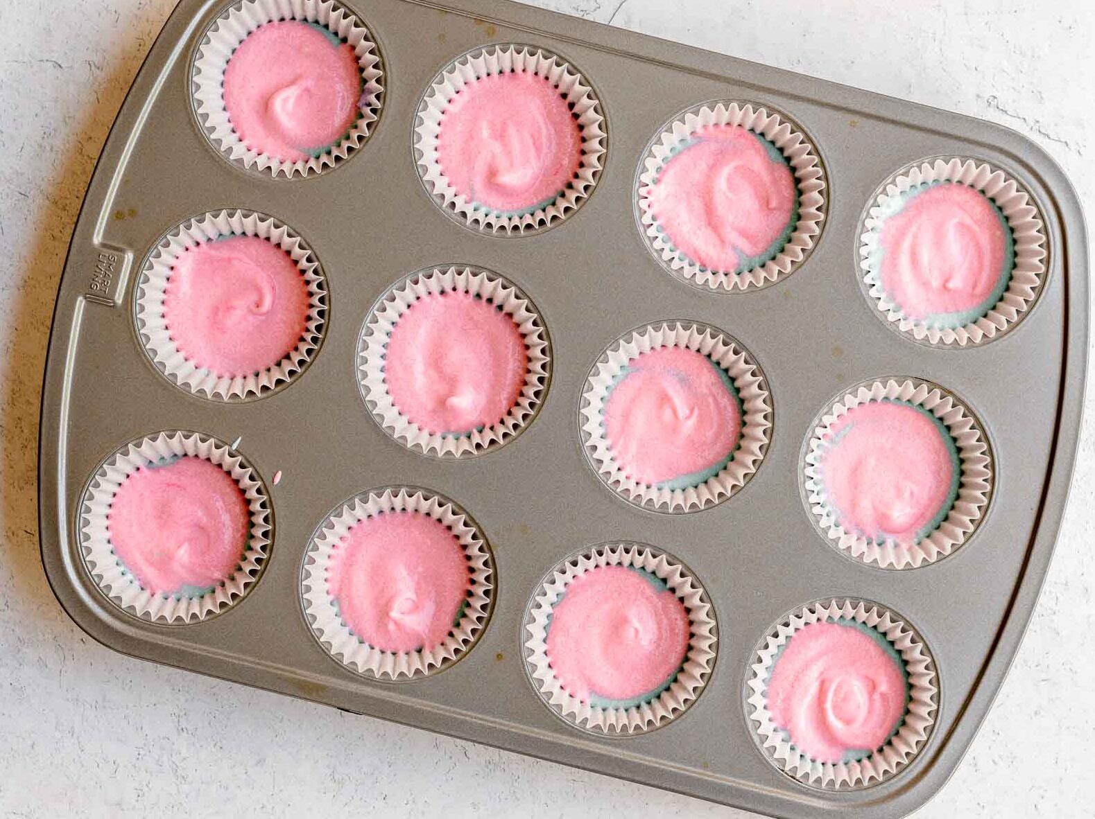Unicorn Cupcakes pink batter over blue and purples batter layers in cupcake pan.