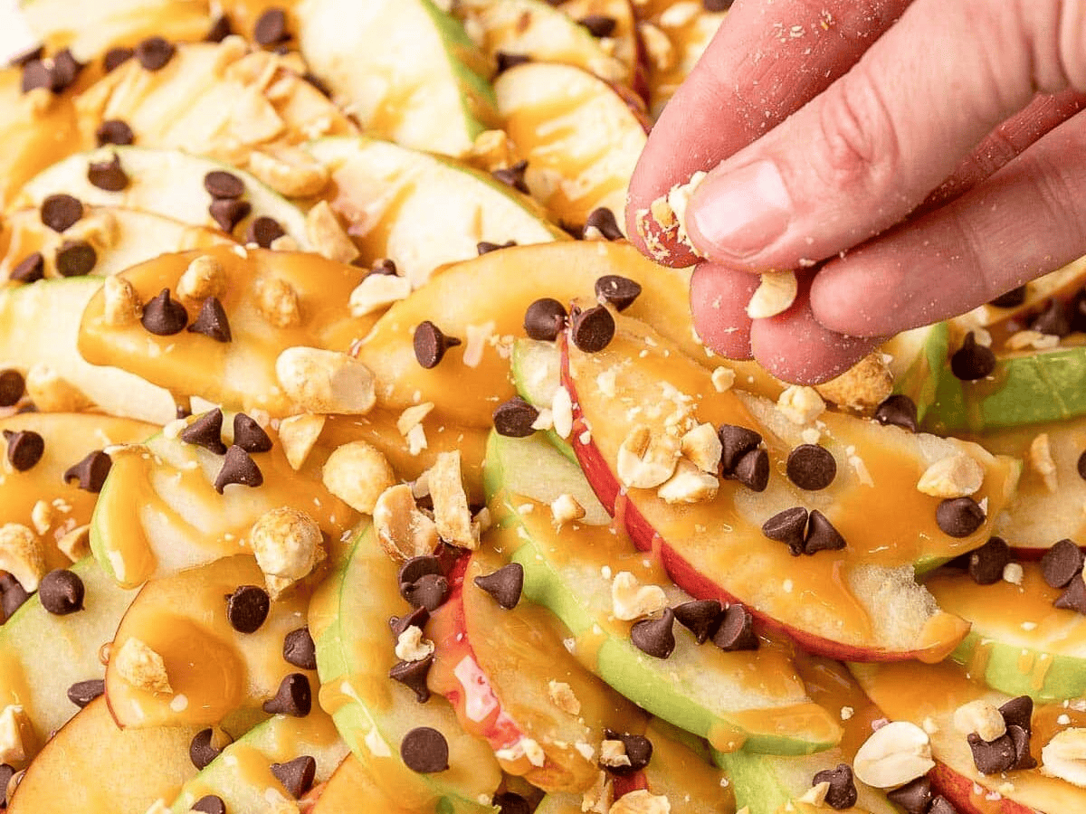 sprinkling peanuts over caramel and chocolate chip covered apple slices on plate