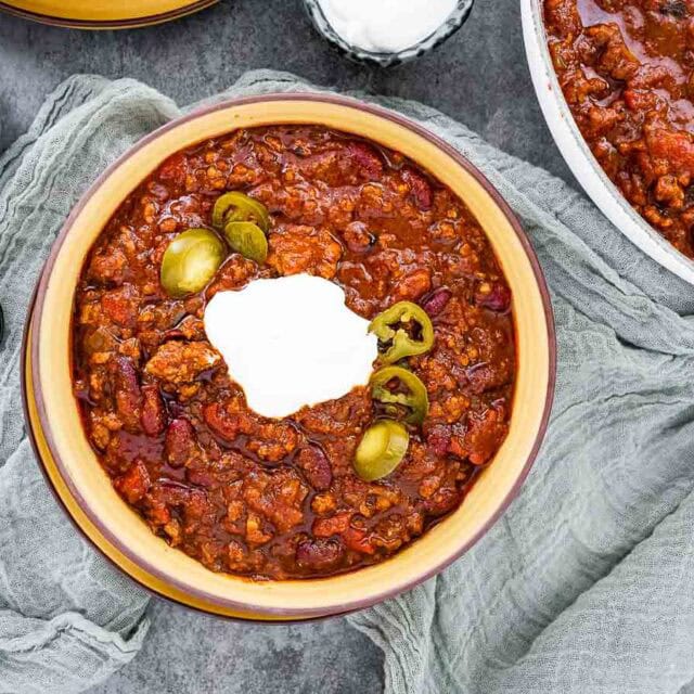 Prepared chili in a bowl with sour cream and jalapenos.