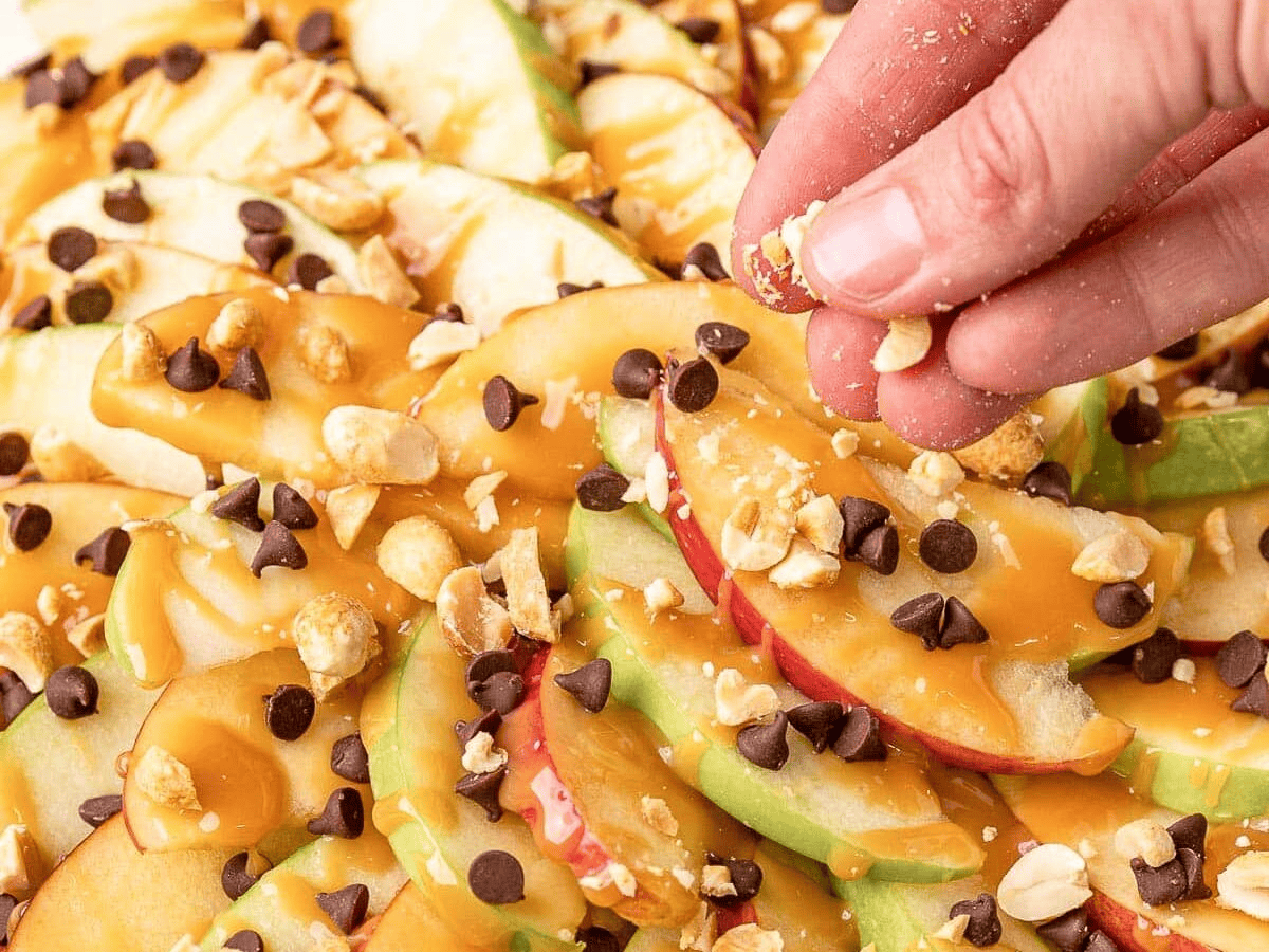 Sprinkling peanuts over caramel apple slices