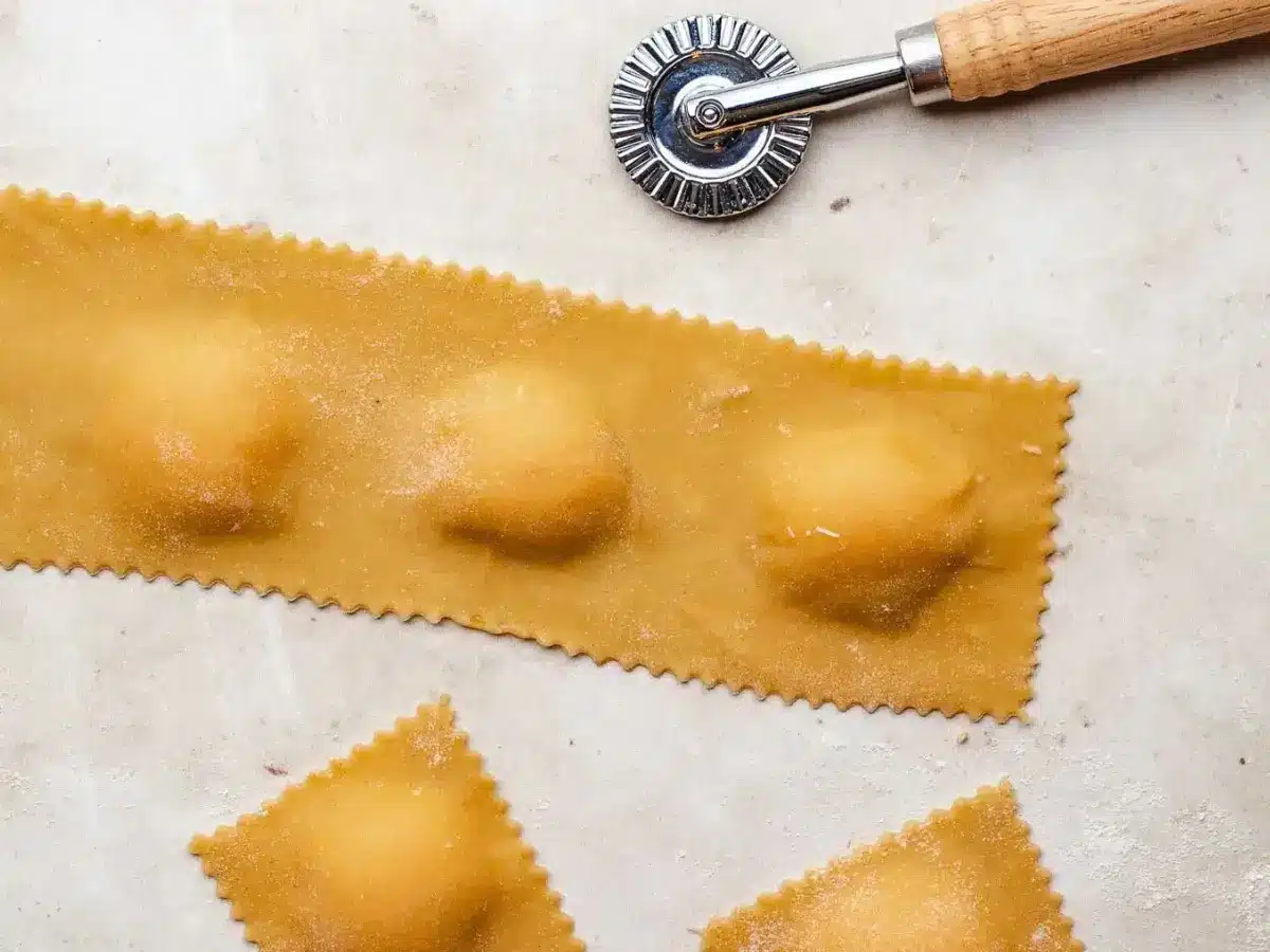Ravioli before its cut on white table next to cutter