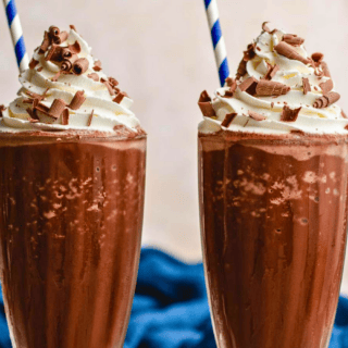 Side by side cups of hot chocolate with whipped cream and straws
