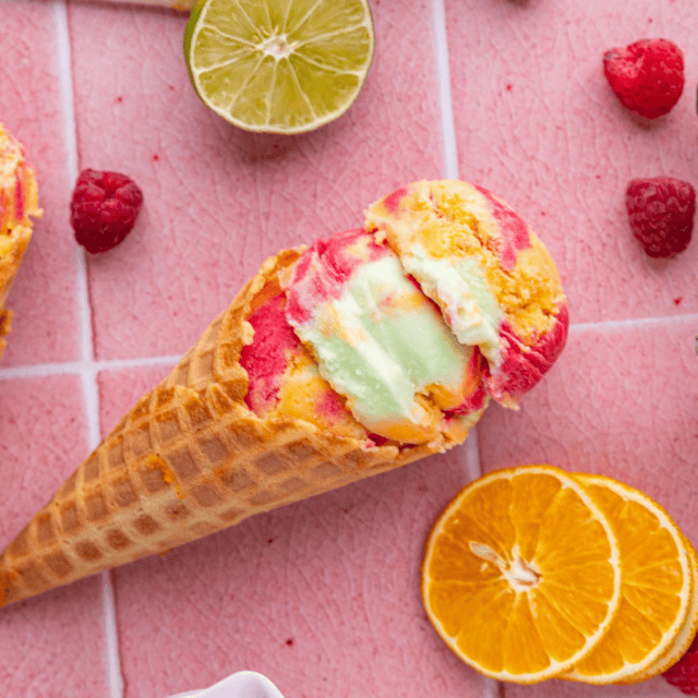 Colorful frozen dessert scooped into a waffle cone surrounded by citrus slices.