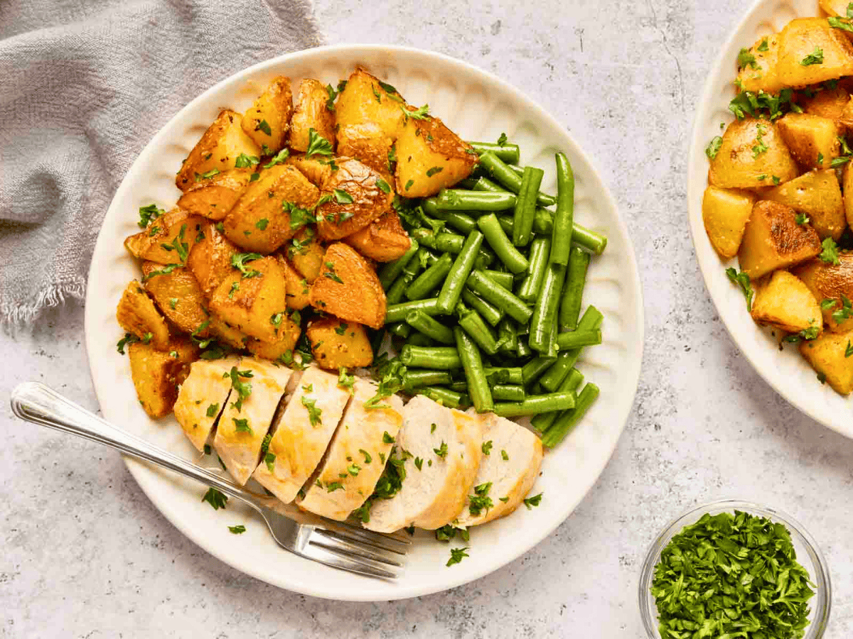 cubed seasoned potatoes on a white plate with green beans and other foods