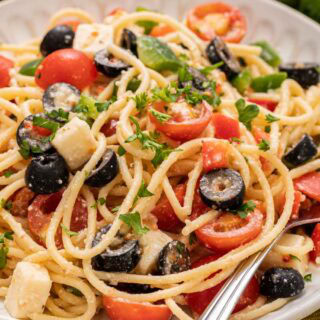 Pasta salad with tomato and black olives on dinner plate with fork.