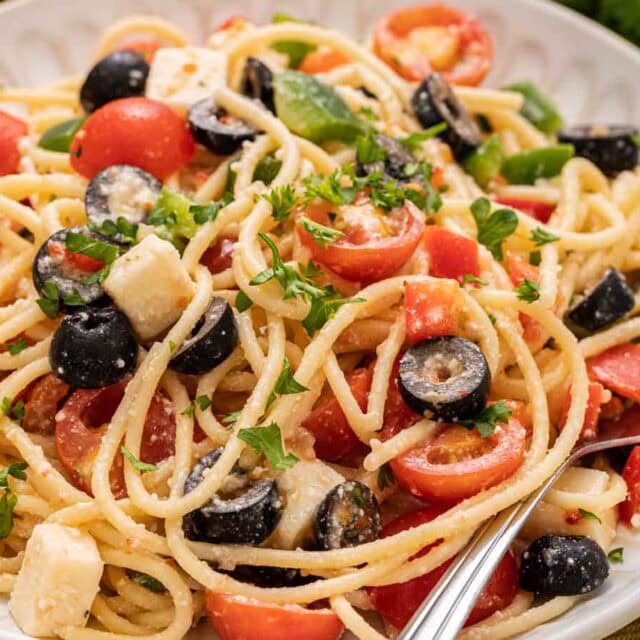 Pasta salad with tomato and black olives on dinner plate with fork.