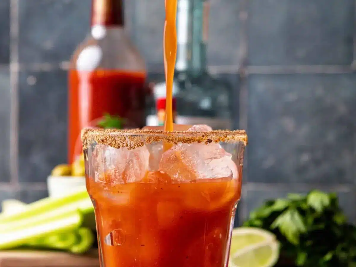Tomato juice pouring into glass with ice.