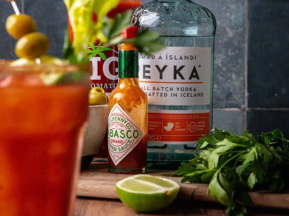 Vodka and tabasco bottles in background of tomato juice cocktail.