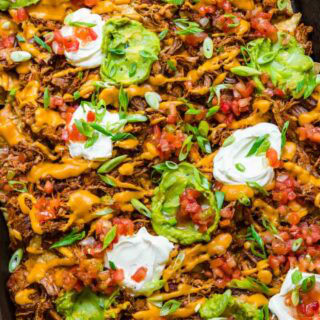 Close up of nachos with sour cream and guacamole on top.