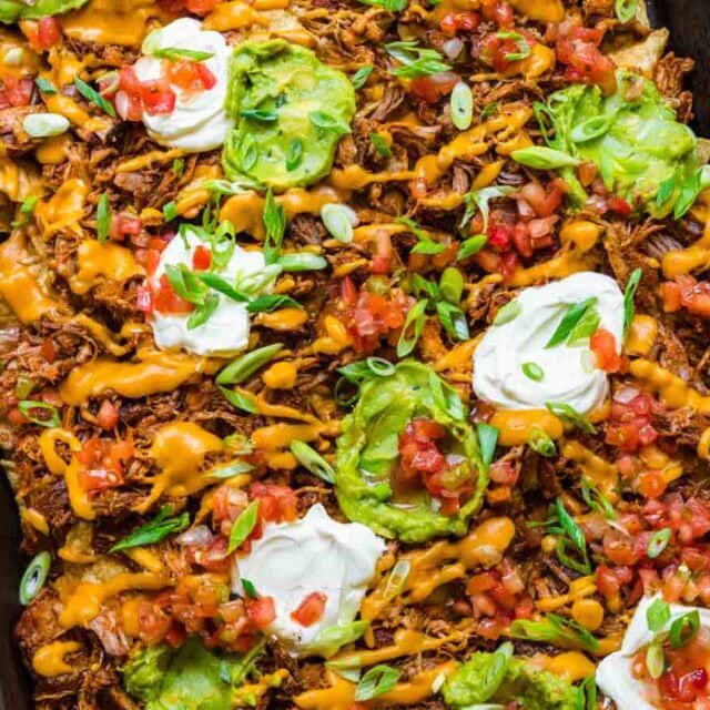 Close up of nachos with sour cream and guacamole on top.