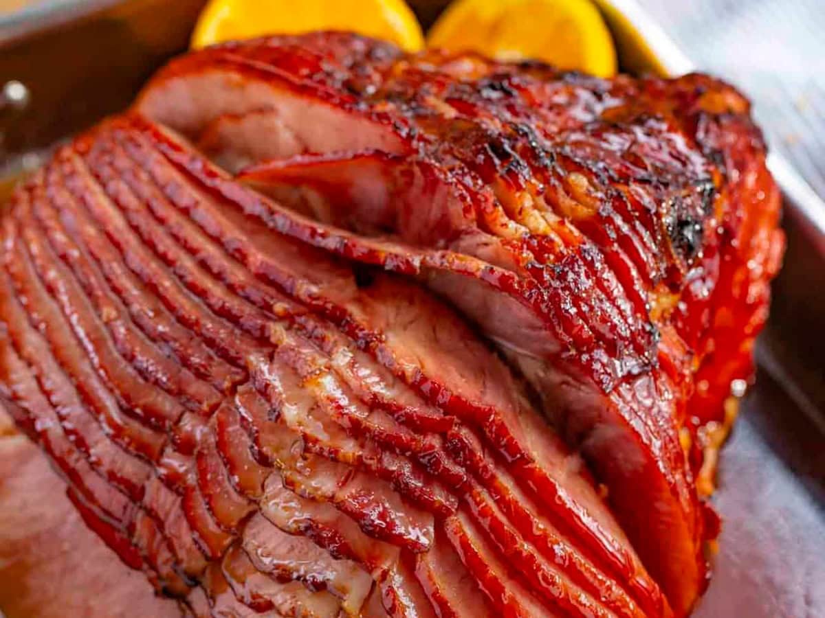 Baked Ham with Brown Sugar Glaze with orange juice, honey, and spices is the perfect sweet and savory flavor combo. Classic holiday recipe! Close up shot of glazed ham in a pan