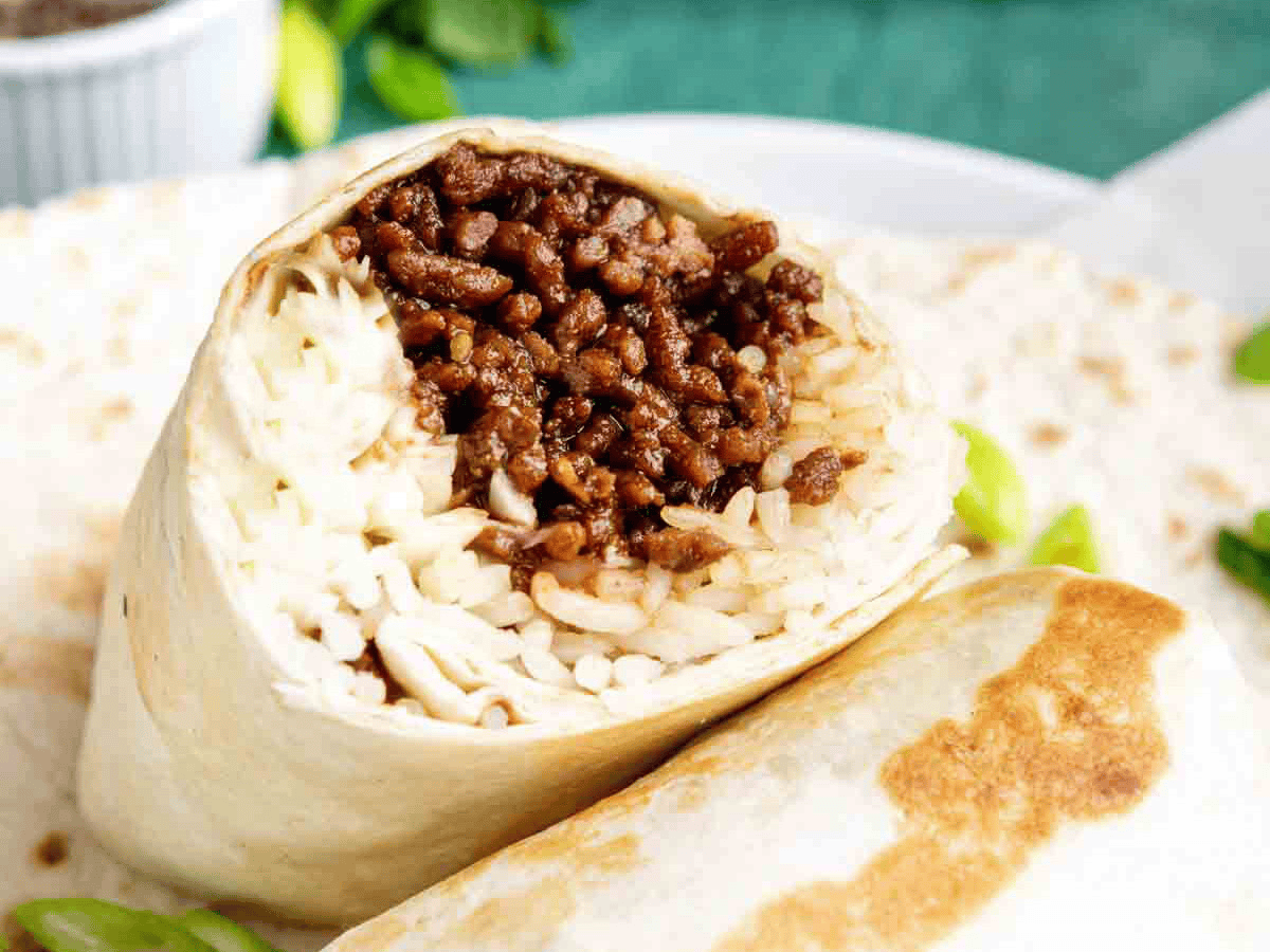 Beef and rice wrapped in a tortilla on a white plate.