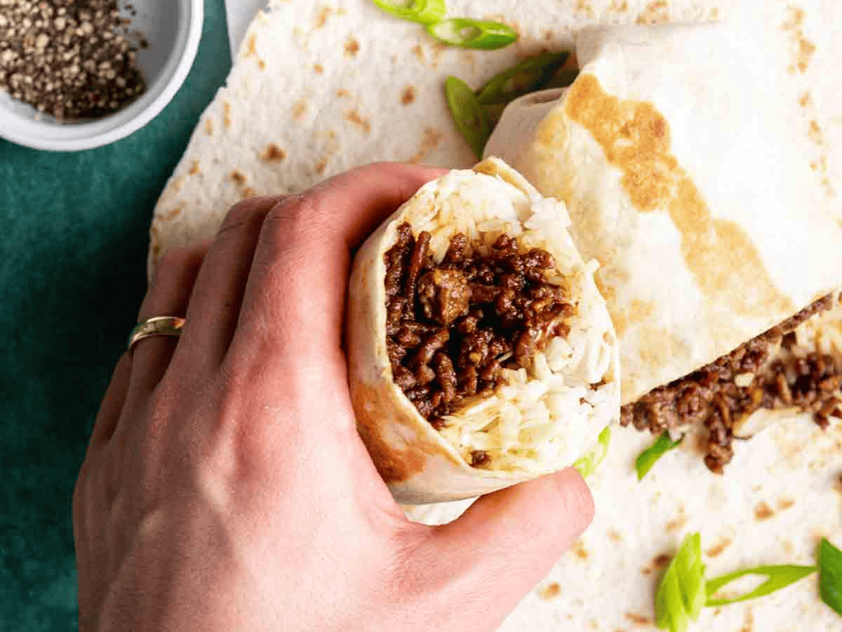 Finished burrito cut in half and being held by someone's hand. 