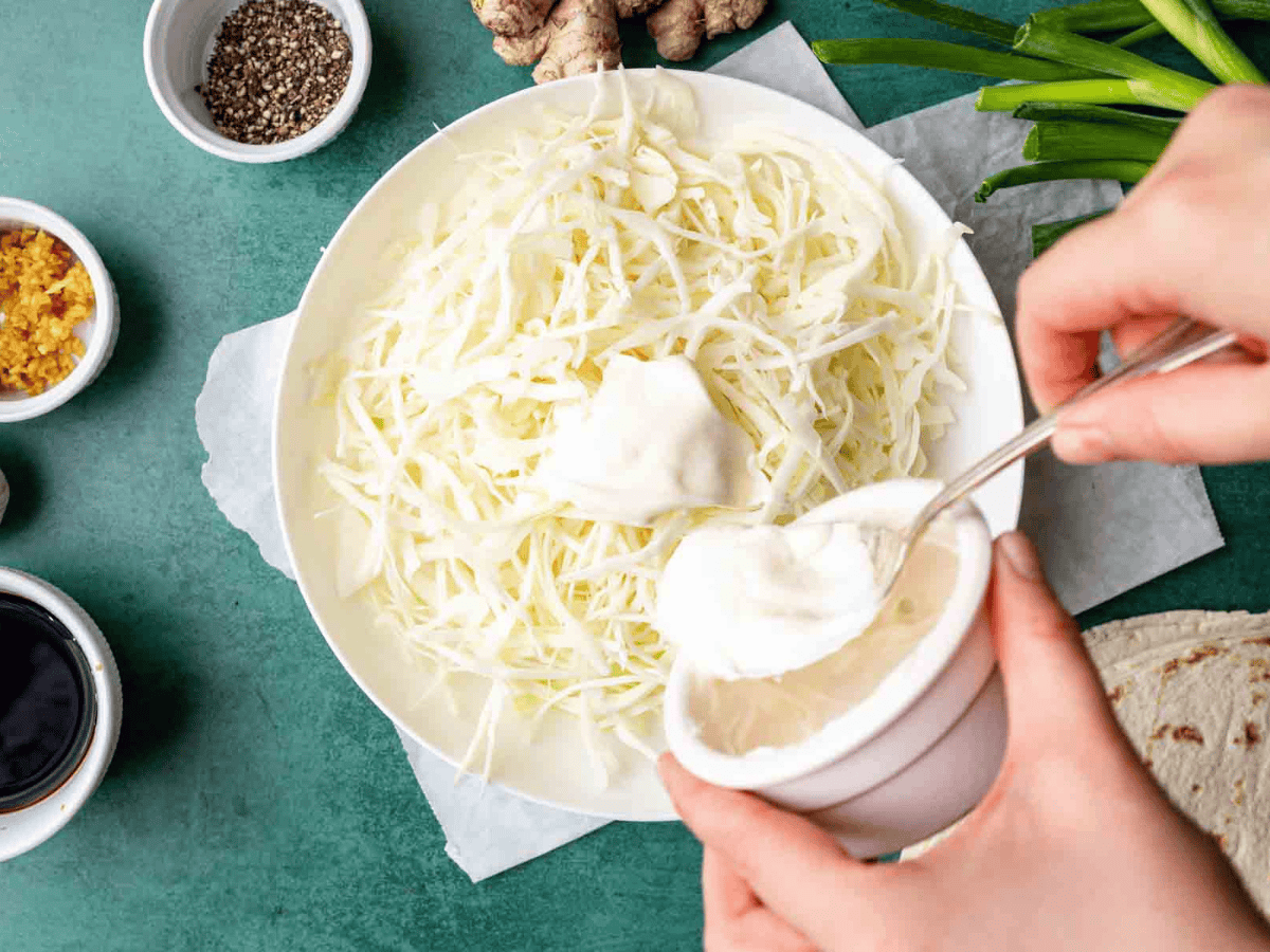 White colored ingredients being spread out on a tortilla.