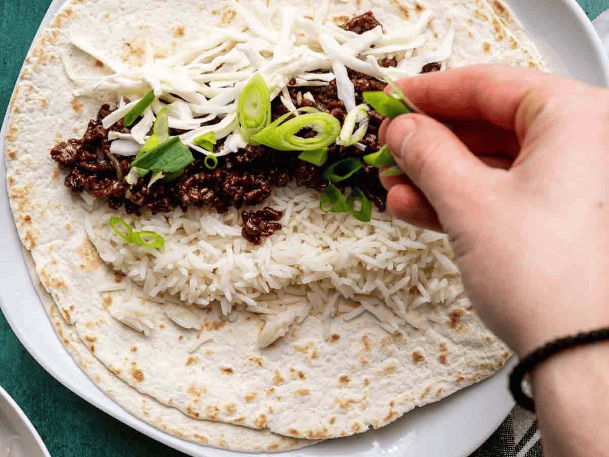 Rice, beef and vegetables being placed on a tortilla.