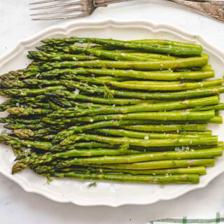 Baked asparagus on a large serving dish with fork.