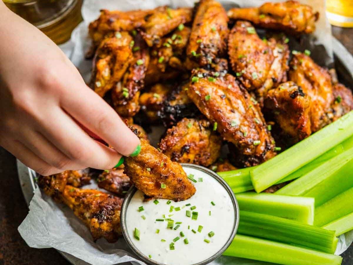 Baked Chicken Wings are made easy, and crispy, in the oven with a tasty spice rub made from chili powder, garlic powder, and onion powder. The perfect appetizer for your next party! Dipping wing into ranch on platter with more wings