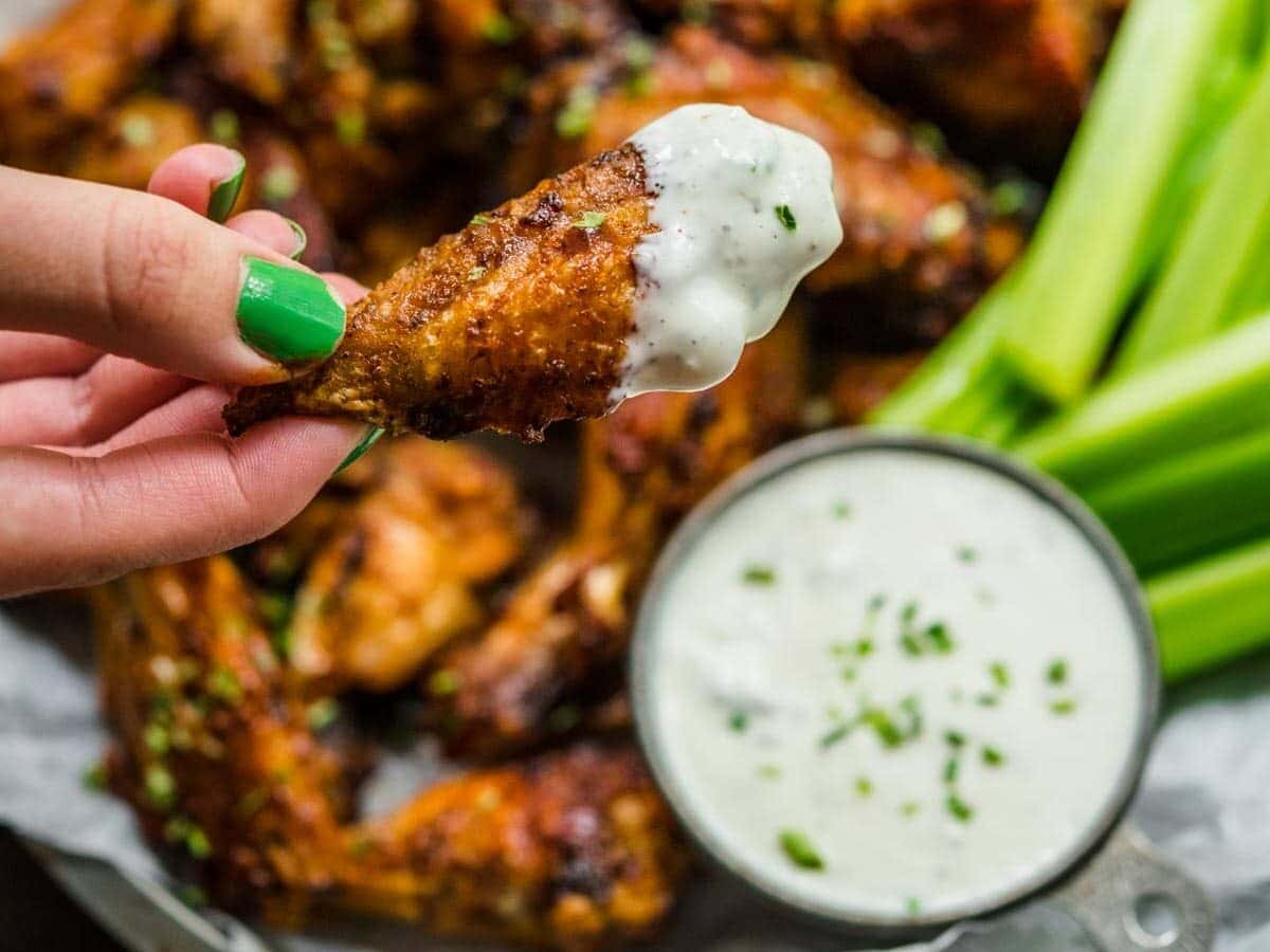Baked Chicken Wings are made easy, and crispy, in the oven with a tasty spice rub made from chili powder, garlic powder, and onion powder. The perfect appetizer for your next party! close up on chicken wing with creamy dipping sauce
