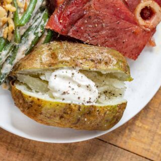 Cooked potato with sour cream plated with ribs and green beans.