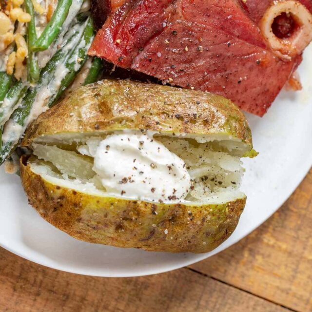 Cooked potato with sour cream plated with ribs and green beans.