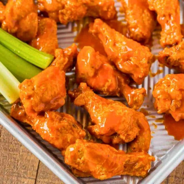 Crispy baked wings with celery sticks on baking sheet.