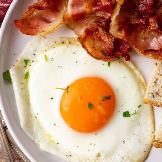 Sunny side up egg on plate with bacon.