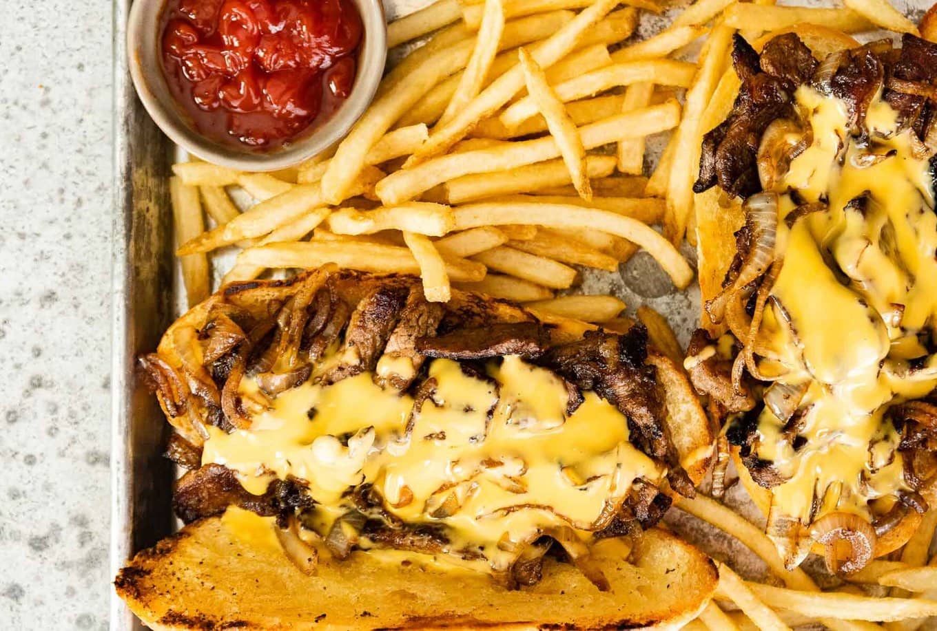 Two sandwiches on platter with cheese sauce and fries