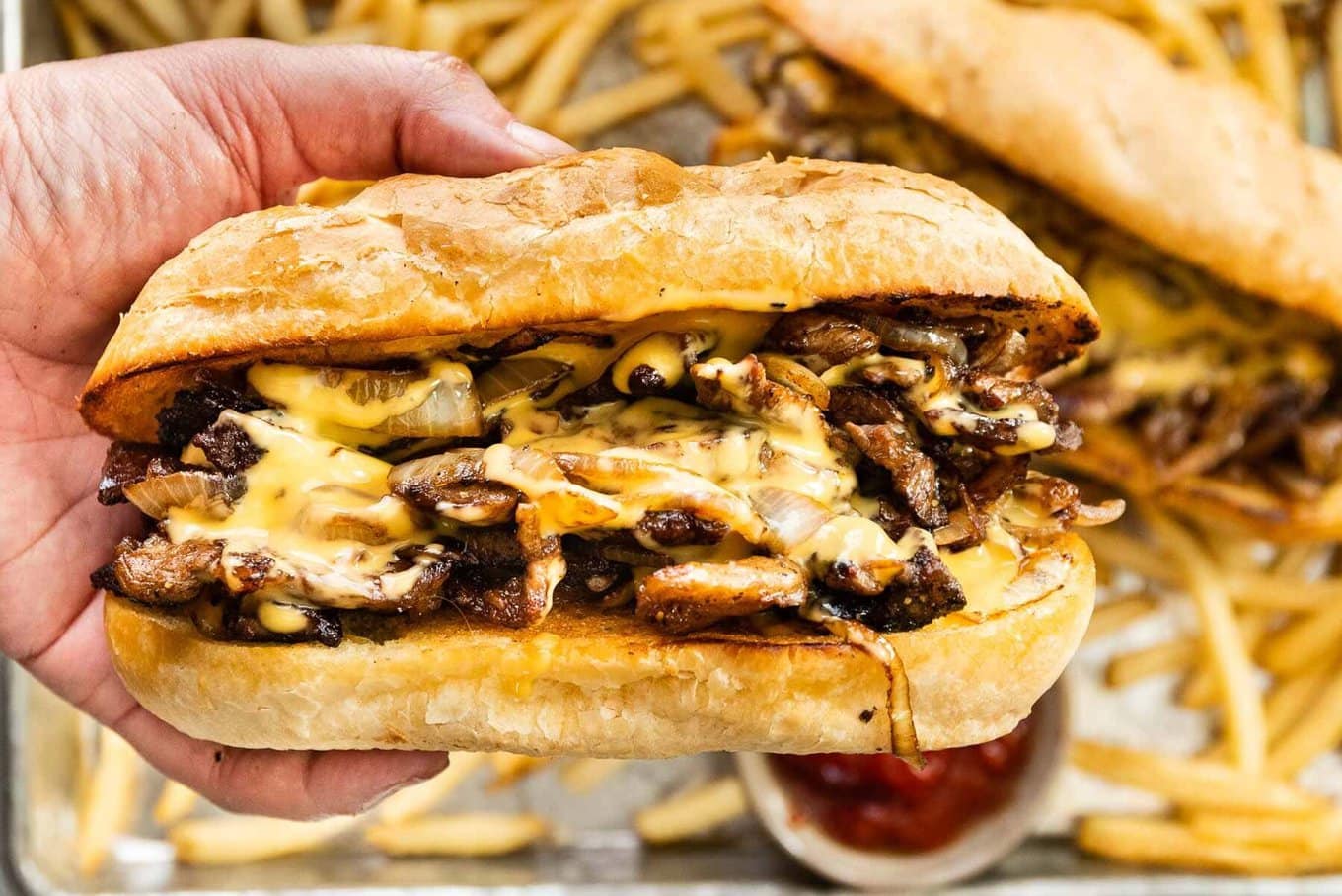 Assembled sandwich in hand over platter with fries and sandwiches