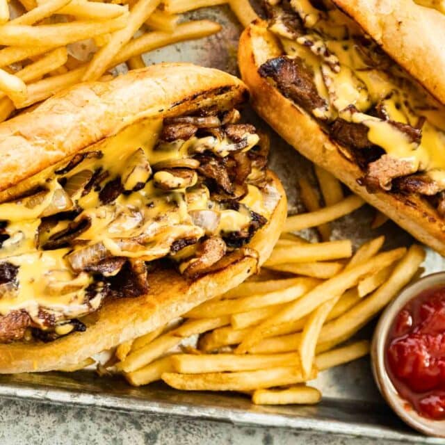 Two assembled hoagies on platter with fries