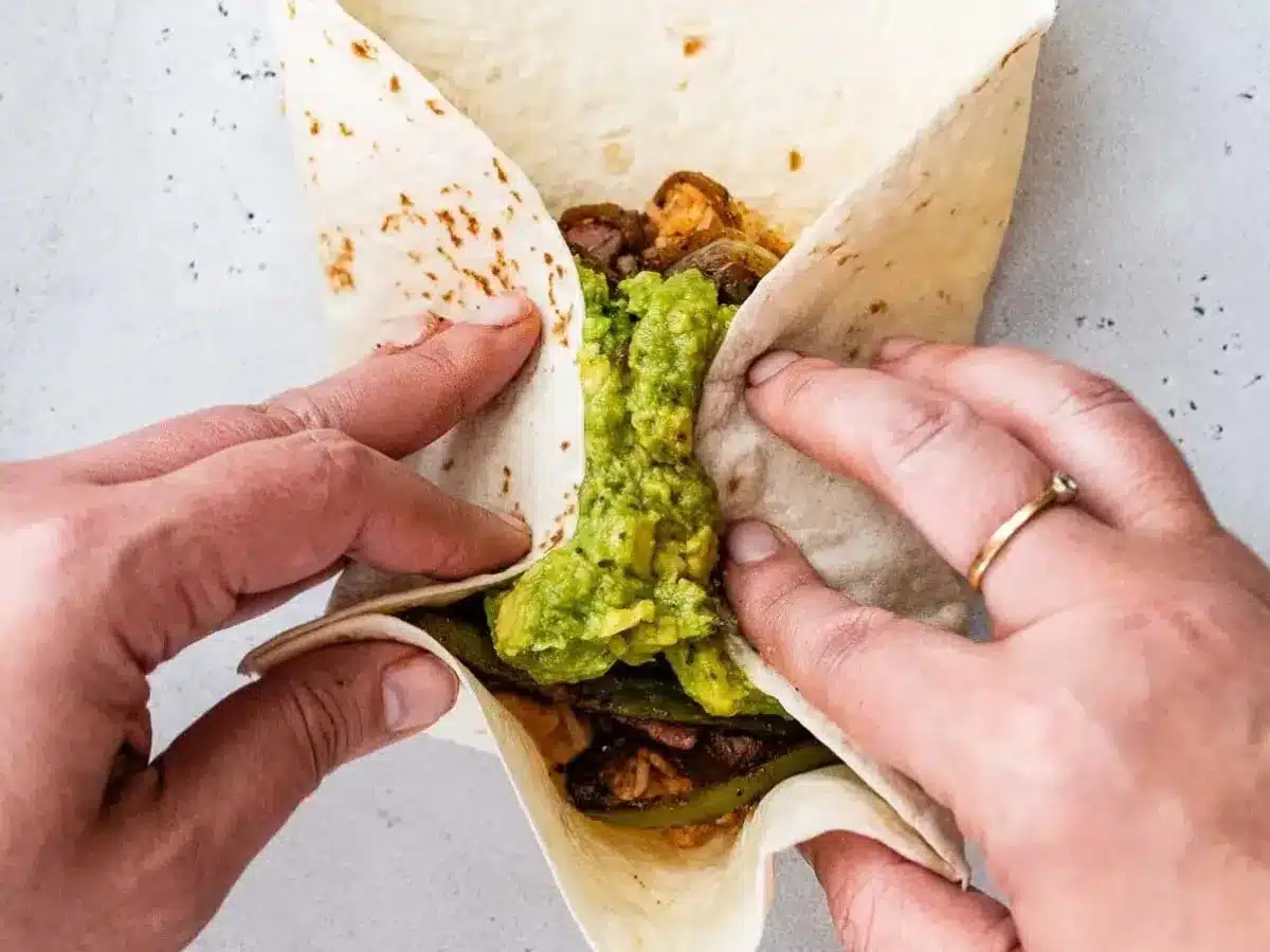 Rolling up tortilla filled with rice, steak, and guacamole 