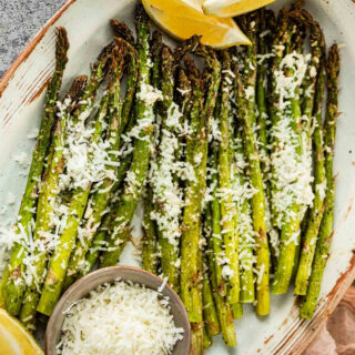 Plate of cooked asparagus topped with cheese with lemon wedges