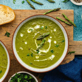 Bowls of soup on wooden board, garnished with cream and asparagus tips