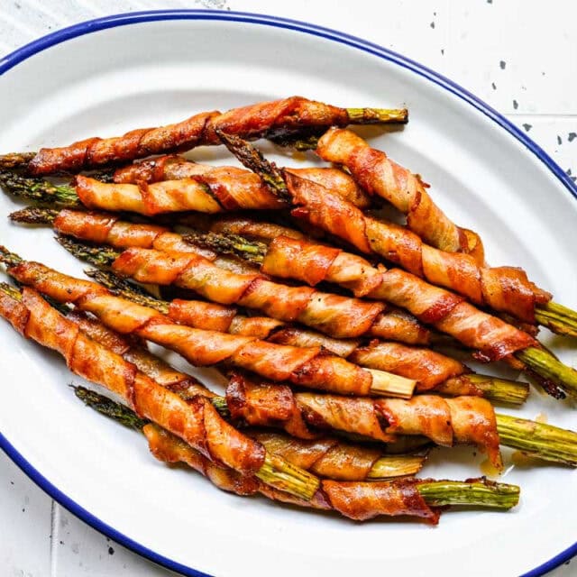 Plate of cooked asparagus wrapped in bacon after baking.
