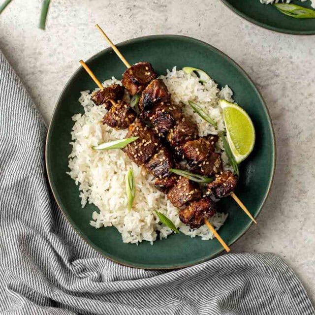 Plate with rice topped with 2 beef skewers