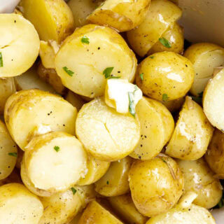 Cooked halved potatoes in bowl with seasonings and butter