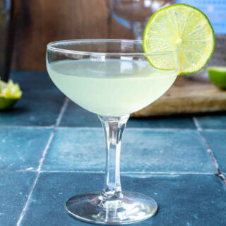 Closeup side view of cocktail in coupe glass with lime slice