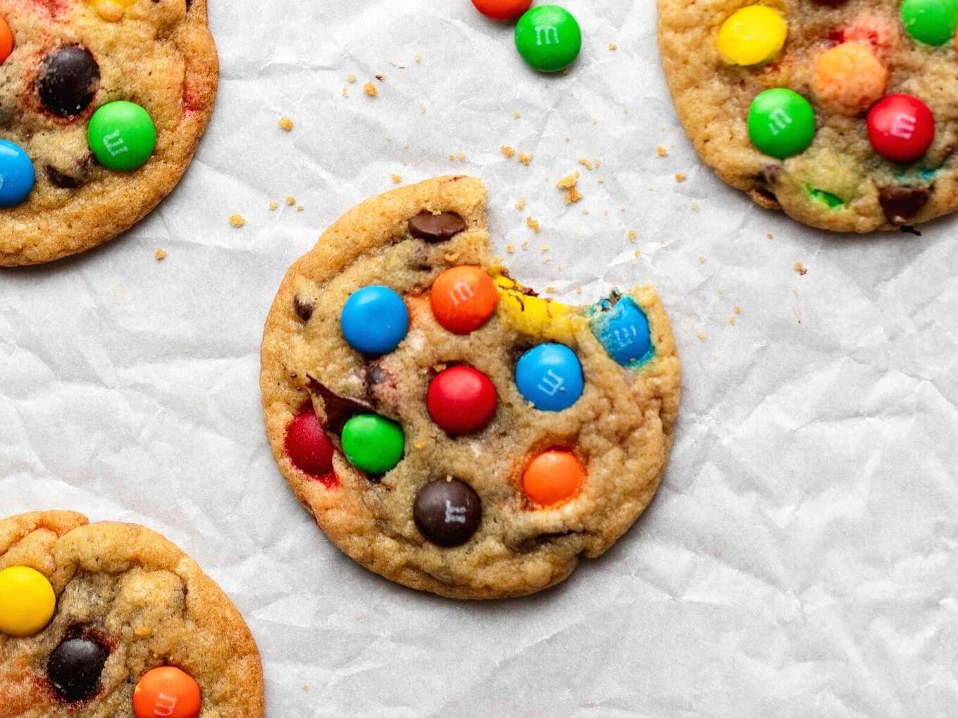 M&M Cookies are soft, chewy, and PERFECT for making ahead of time, made with M&M candies and chocolate chips, and bake in only 10 minutes! A perfect kid-friendly Christmas holiday baking dessert! cookie on baking sheet with bite taken