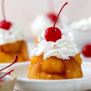 Cupcakes on serving plates with cherry and whipped cream topping.