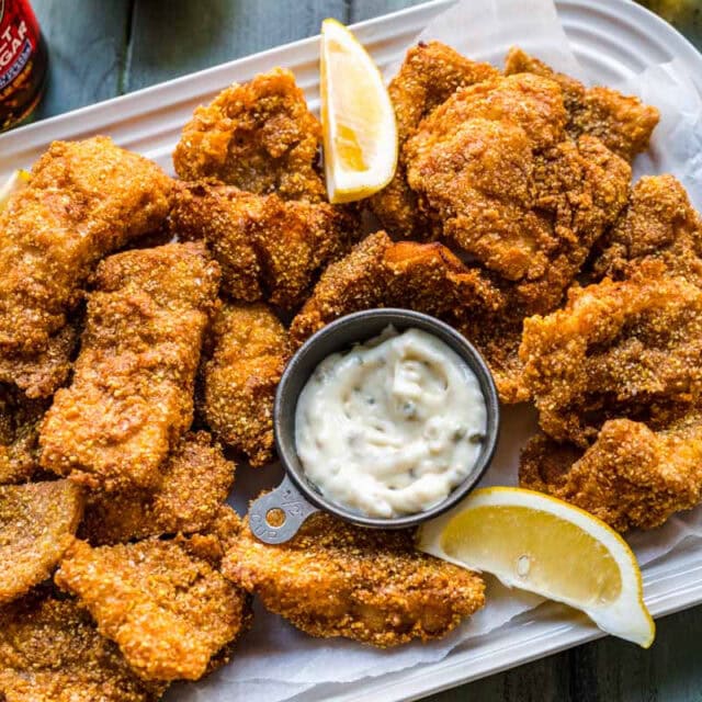 Platter of fried fish pieces with tartar sauce and lemon wedges