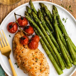 Cooked asparagus on plate with baked chicken and tomatoes