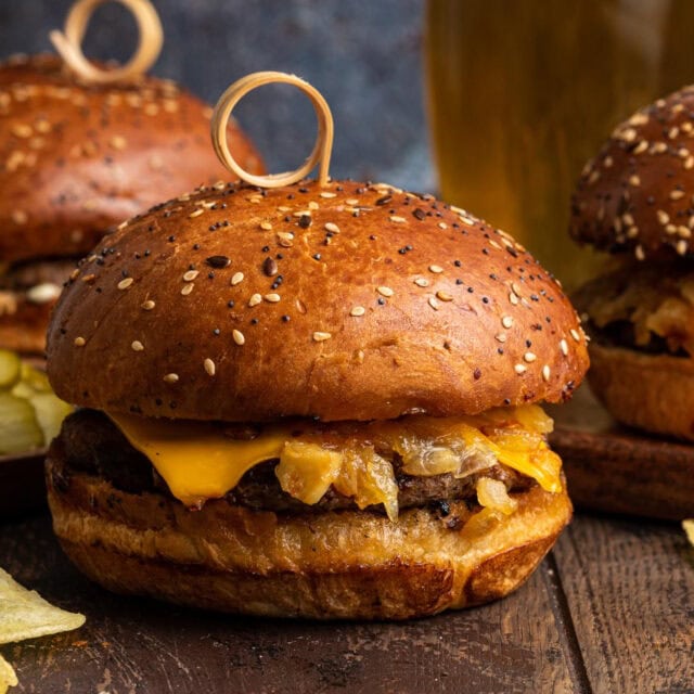Assembled burgers with cheese and onions on wooden board.