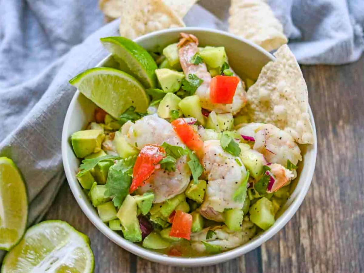 This easy Shrimp Ceviche recipe is a classic Mexican dish full of flavor with fresh shrimp, veggies, avocado and spices. Great for summer! Bowl of finsihed ceviche with garnishes