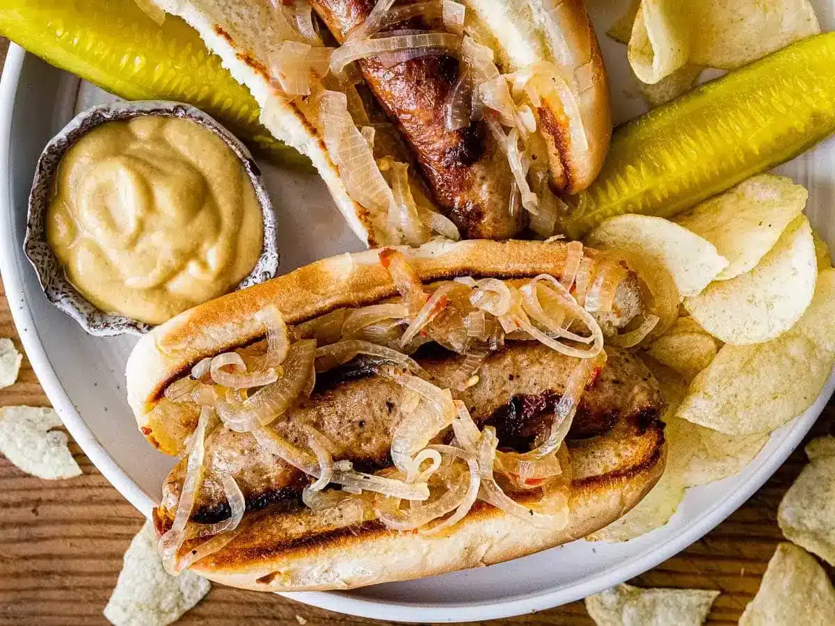 plate of 2 sausage sandwich with pickles and mustard