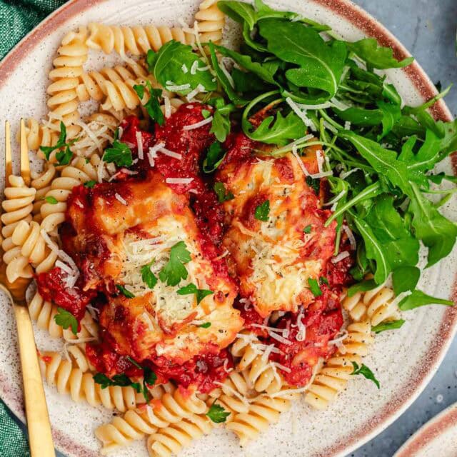 Cheesy eggplant on a bed of pasta on dinner plate.