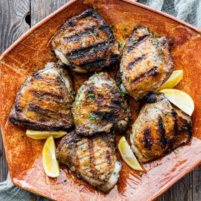 Grilled thighs on serving plate with lemon wedges