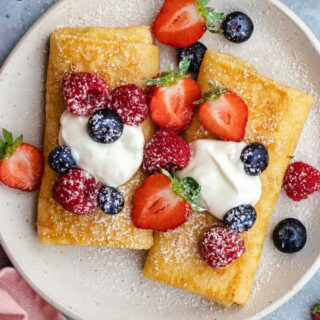 Blintzes on plate with fresh berries, sour cream, and powdered sugar.