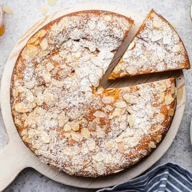 Cake in white dish with powdered sugar and almonds on top