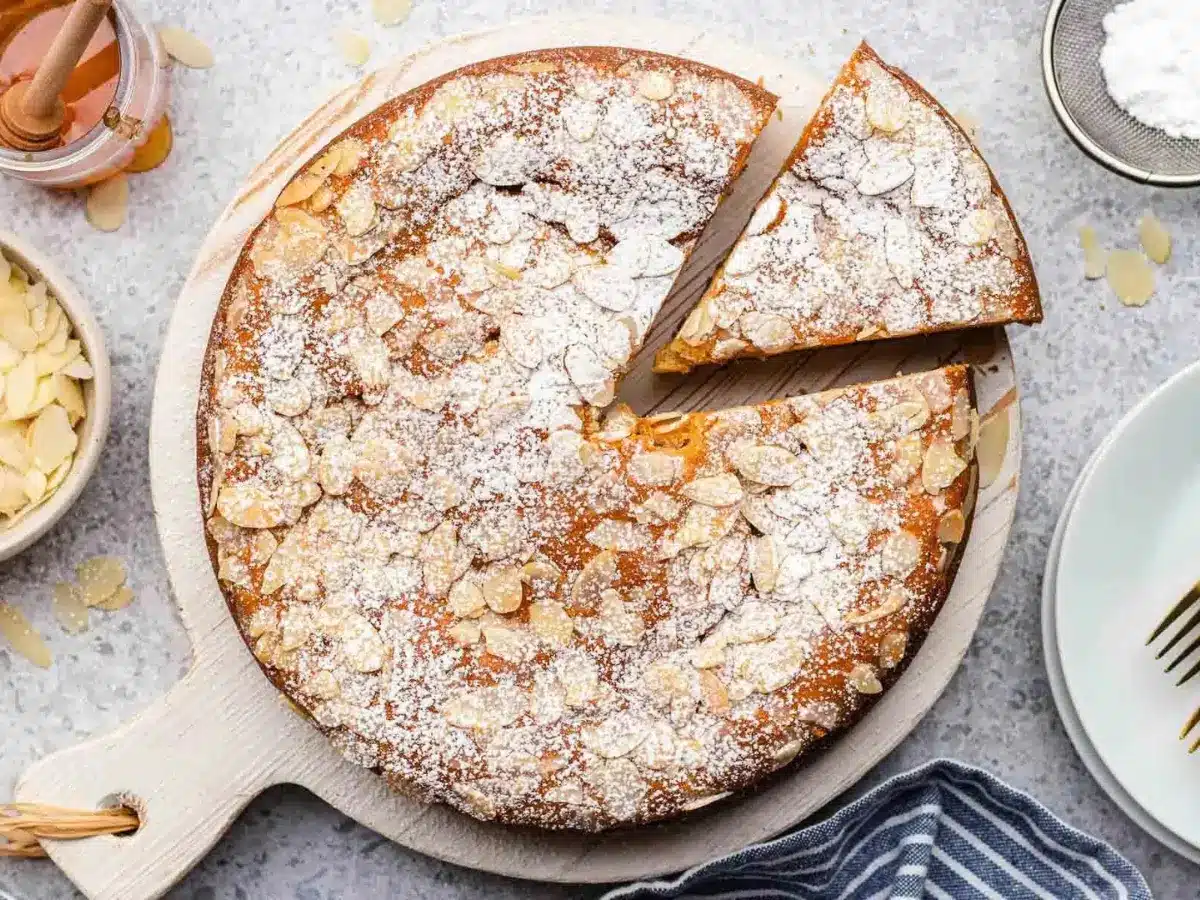 Cake in white dish with powdered sugar and almonds on top