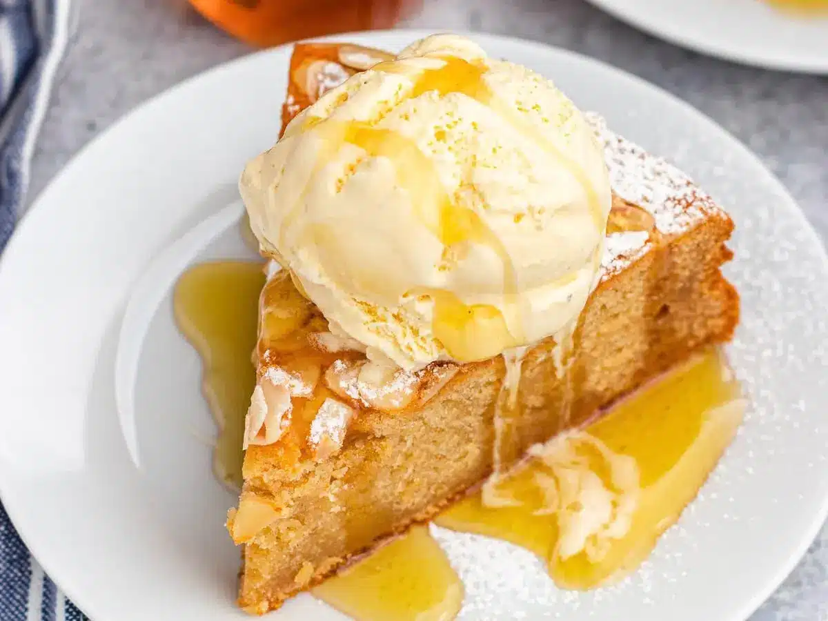 Slice of cake on white plate with ice cream and honey on top